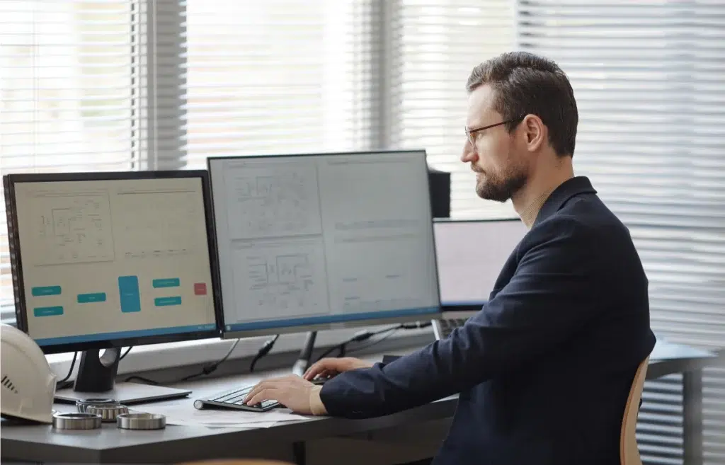 Bearded male engineer using computer with blueprints on screen in office