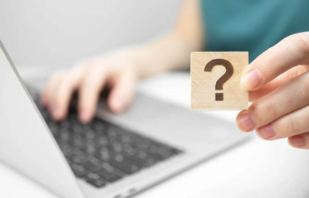 Customer care and support concept background faq question mark icon on a wooden cube closeup view laptop on a white office table photo